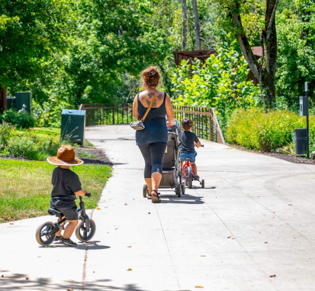 Sunny day on a paved trail with a mom pushing a stroller and kids riding bikes.