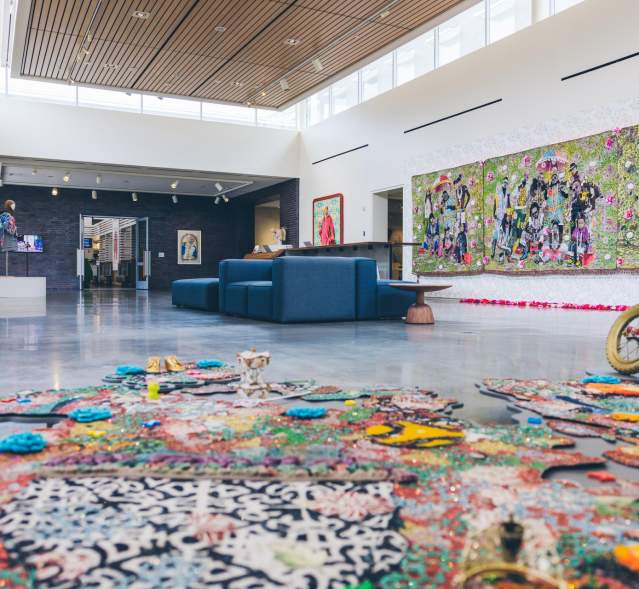 A spacious art gallery featuring vibrant wall murals and colorful floor installations. Modern seating is visible, enhancing the creative atmosphere.