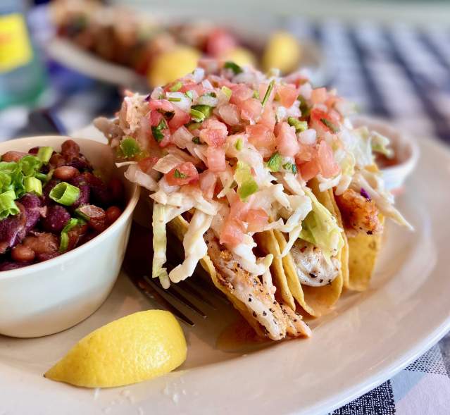 A plate of fish tacos with a side of black beans.
