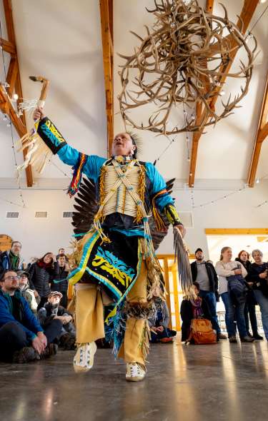 An image of a Native American dancer performing in front of a crowd indoors at Aldo Leopold Nature Center.