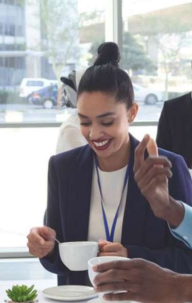 A white man, Black man, and Asian woman in professional attire talk and laugh while drinking coffee at a meeting.