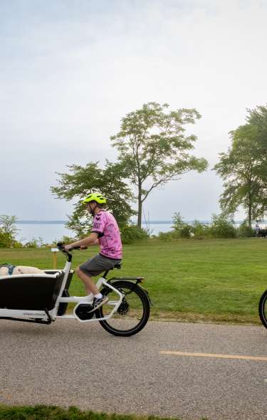 A man riding a bike with an attachment at the front for his dog and a woman riding her bike behind him on the LakeMonona Loop.