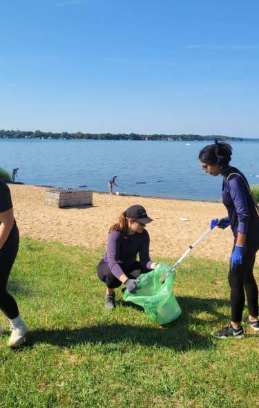 Three women clean up garbage on a beach in Madison, WI