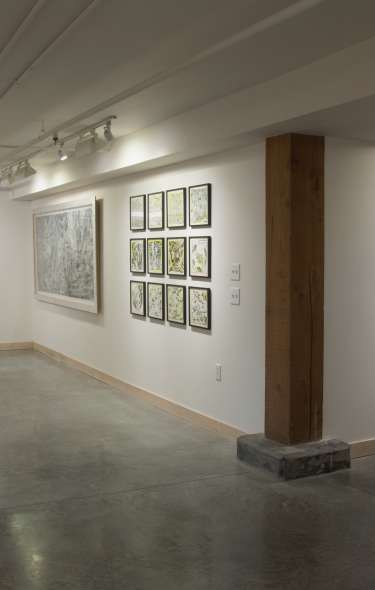 A wide shot of three walls in an art gallery displaying paintings of a variety of sizes and colors