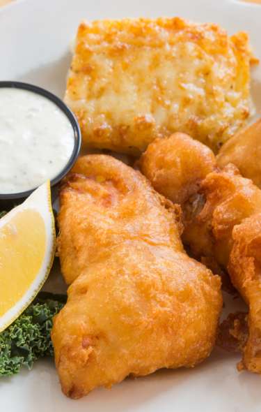 A plate of three pieces of fried fish, bread, a lemon, and dipping sauce from Quiveys Grove