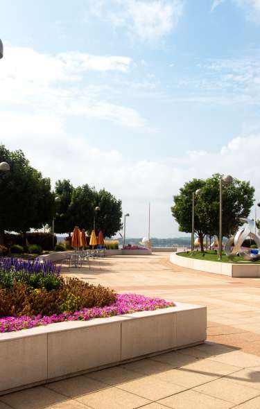 An outdoor patio area at Monona Terrace featuring sculptures and raised garden beds with the lake in the background.