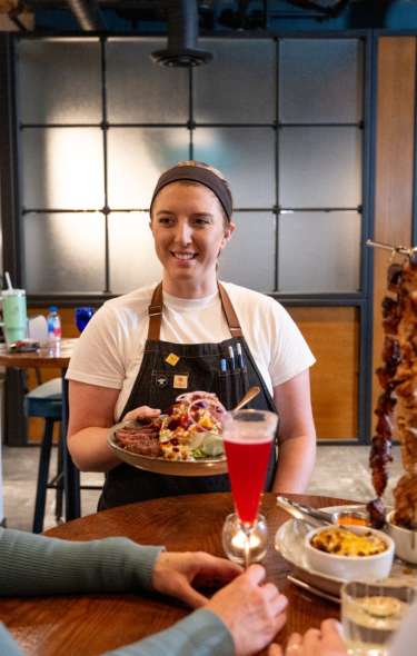 A white woman serves a plate of food at a hotel restaurant to a white man and white woman
