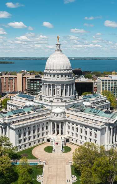 Aerial shot of the Wisconsin State Capitol building. Blue skies are overhead and a lake sits at the back of the photo.