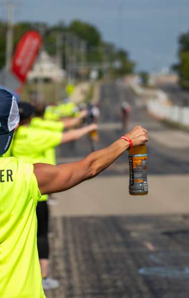 An image of a person volunteering at Ironman, handing a drink off to a biker