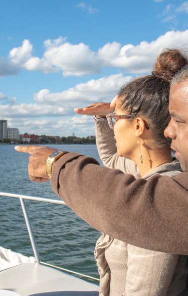 A Black man and woman look out toward the Madison skyline while riding a boat on one of Madison's lakes