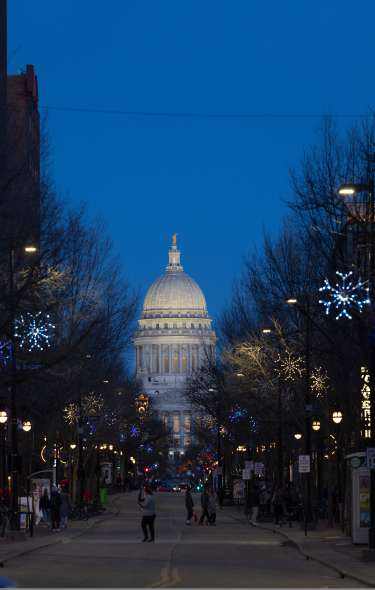 An image of downtown Madison in the winter at night with the Capitol lit up at the end of the street.
