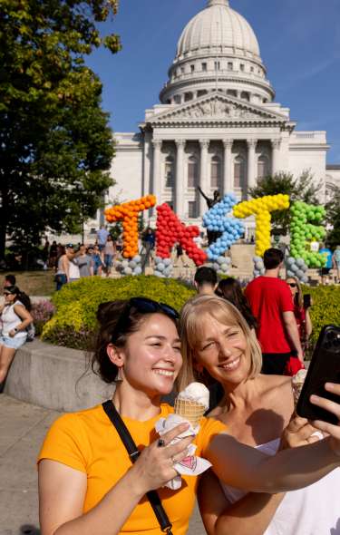 Two women taking a selfie in front of the "Taste of Madison" sign on the Capitol Sqaure