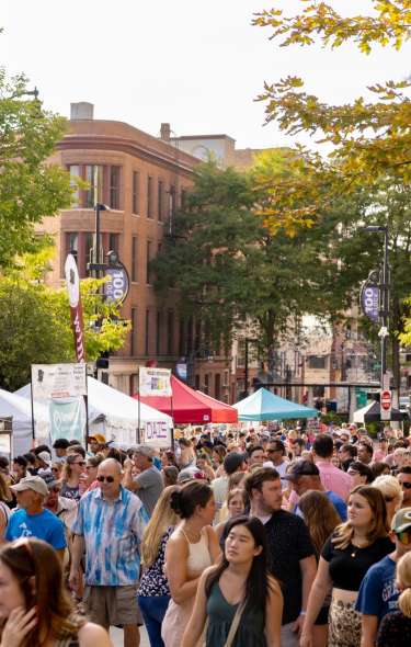 A crowd of several dozens of people walk around Capitol Square and stop at booths with food at Taste of Madison