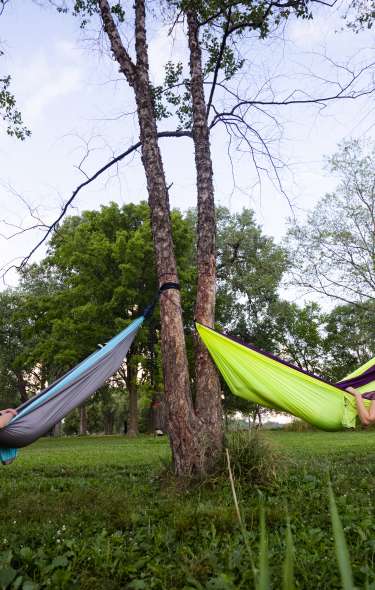 Two people lay in hammocks looking toward each other in a park.