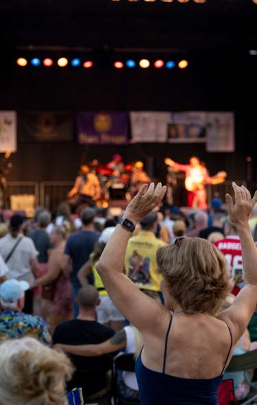 An image of an people up and dancing in front of a stage at an outdoor music festival.