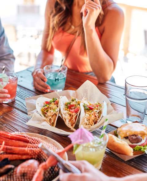Friends joined at a table enjoying crab legs, tacos, and beverages.