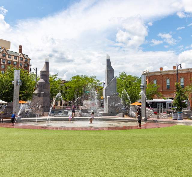 Green grass and an interactive splash patio surrounded by historic buildings in downtown Rapid City, SD.
