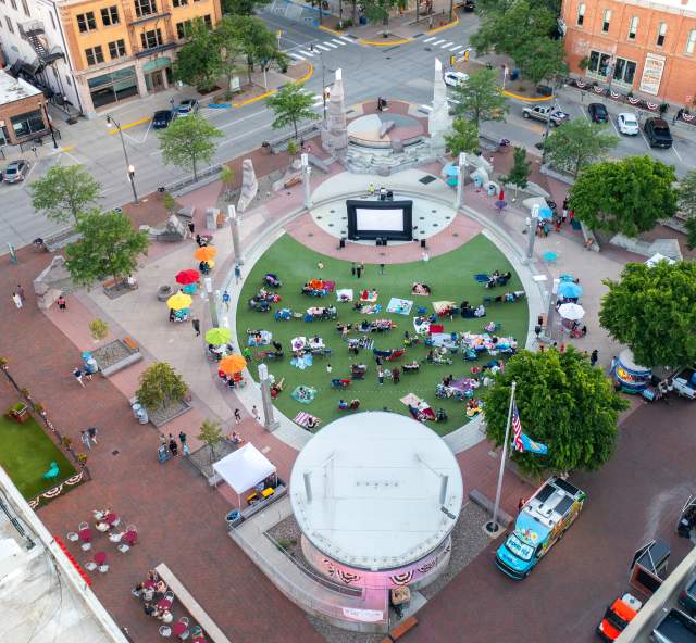 Aerial view of Movies on Main at Main Street Square, where attendees relax on blankets and lawn chairs around an outdoor movie screen in downtown Rapid City.