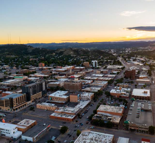 Aerial view of downtown Rapid City at sunset with the Black Hills stretching across the horizon.