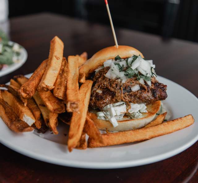 A pulled pork-topped burger with onion and cilantro is served with thick-cut fries at Thirsty’s.