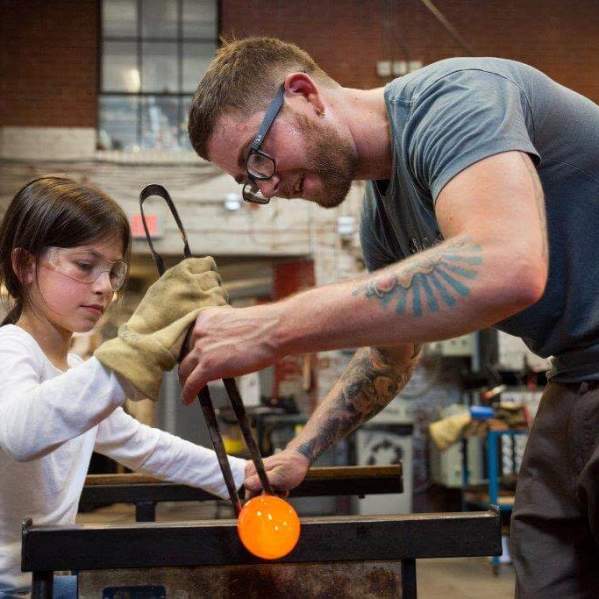 A young girl is being taught to blow glass at the Goggleworks Center for the Arts