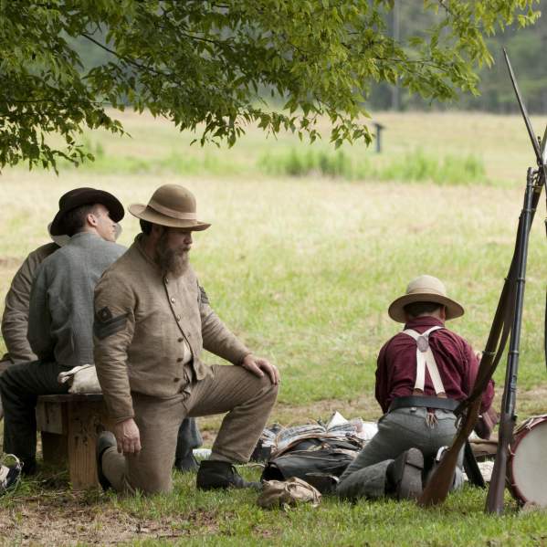 Three men and a boy dressed in historic fire setting up a campsite in a field
