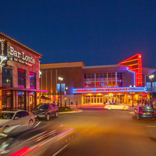 A shopping area at night with neon lights and cars going by