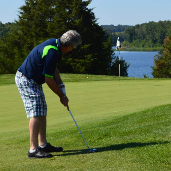 A man playing golf on a gold course with a body of water and trees in the background
