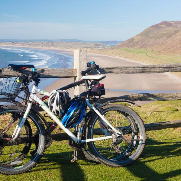 Bikes against a fence with Rhossili Bay in the background.