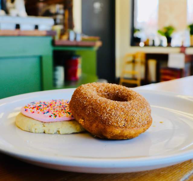 A cinnamon sugar donut and frosted sugar cookie sitting on a white plate in Mud Pie Bakery & Coffee