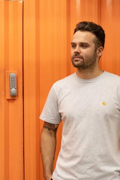 Manchester based artist, Corbin, stood in front of an orange wall.