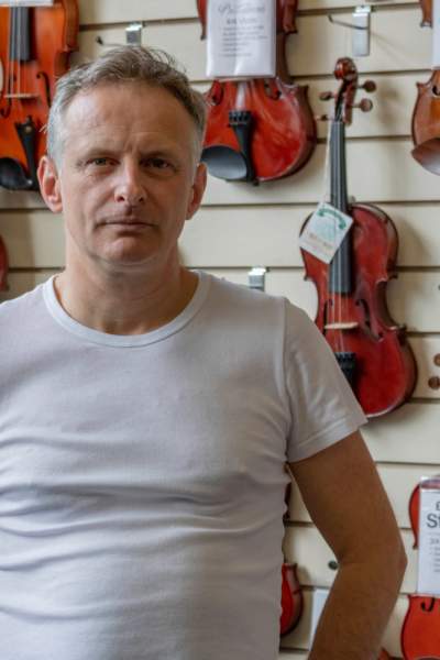 John Roadhouse Jr pictured in front of a wall of violins in his music shop