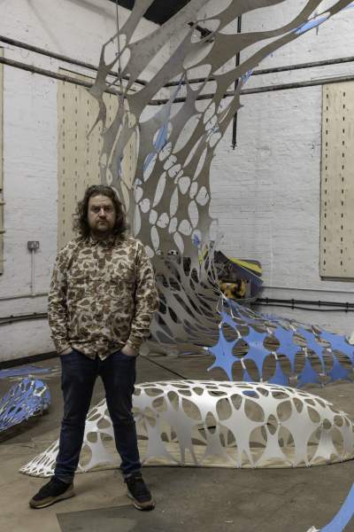 Liam, an artist and sculptor stood behind a blud sculpture