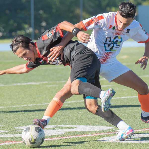 Two male soccer players fighting for a soccer ball on a soccer field.