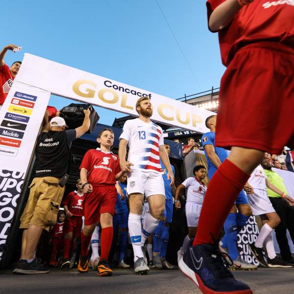 Male soccer players walking onto a soccer field from the stands.