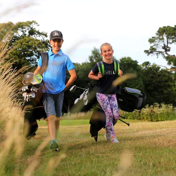 Two young children on a golf course carrying golf bag and clubs