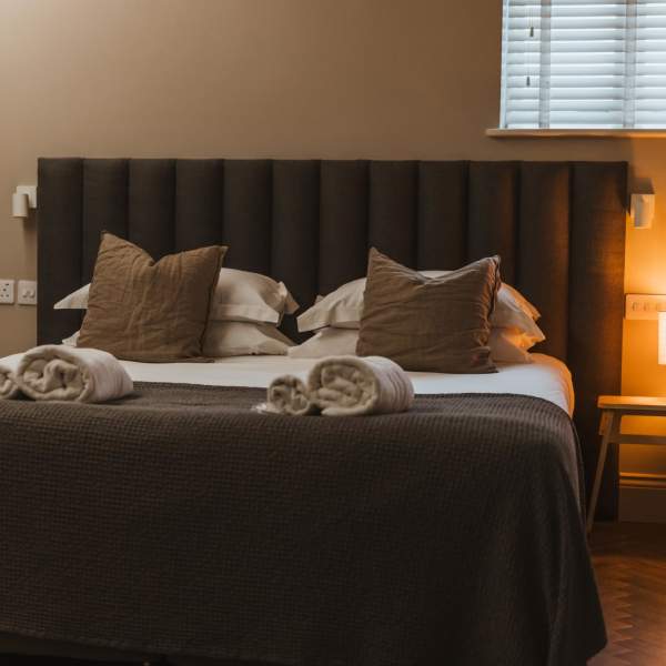 A comfy bed with grey coverings and a light on next to it.