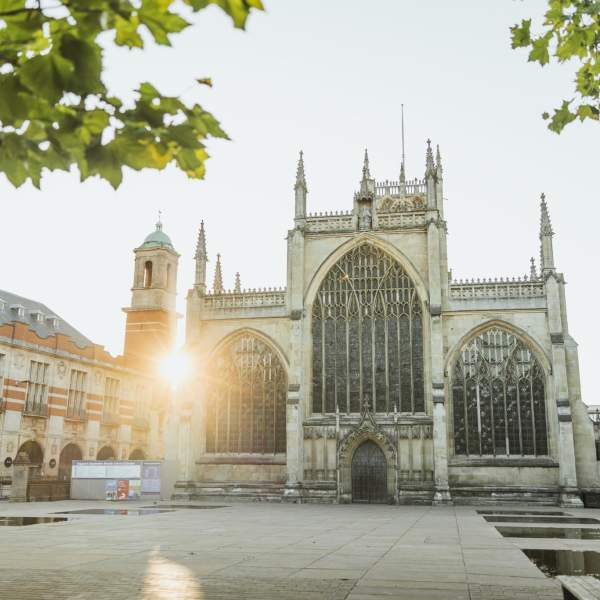 The exterior of Hull Minster at sunrise, a beautifully ornate church with a number of filials with the sun peeking through the edges of the buildings around it.