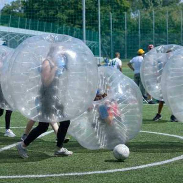 Group of people running on pitch plaing football in zorbing bubbles