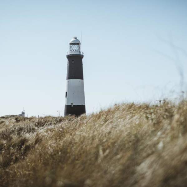 Spurn Point's black and white light house standing above tall dune grass blowing in the wind under a bright blue sky