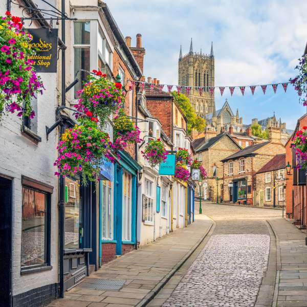 A cobbled street with colourful flowers and cathedral in the background