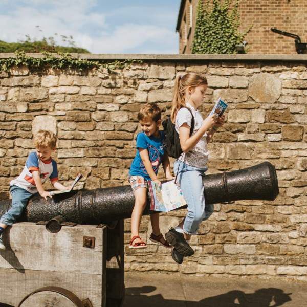 Three children sat on a castle cannon examining a guidebook