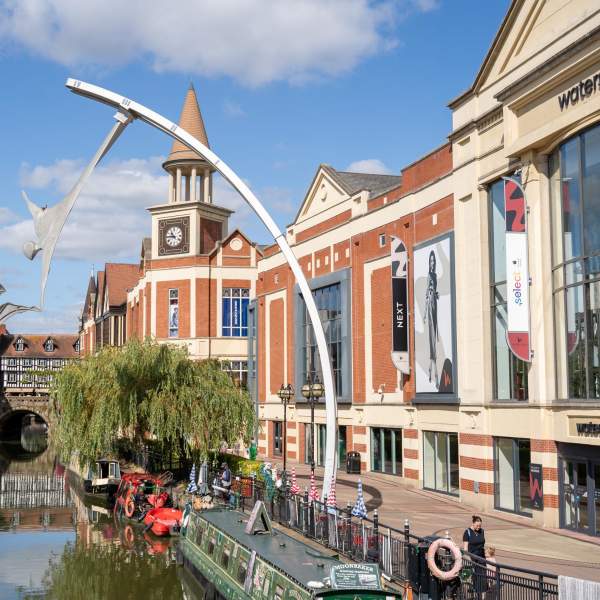 Canal boats on the river through Lincoln with a sculpture of two people touching hands, with waterside shopping centre in the background