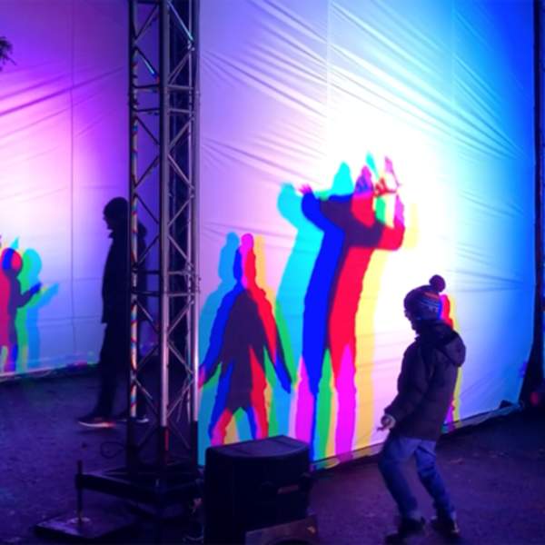 A light installation with children dancing in front and creating shadows