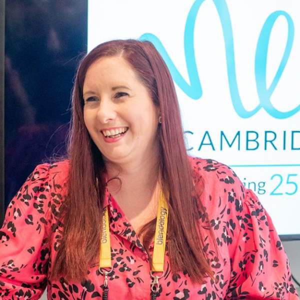 Smiling white woman in floral pink shirt handing over a delegate badge