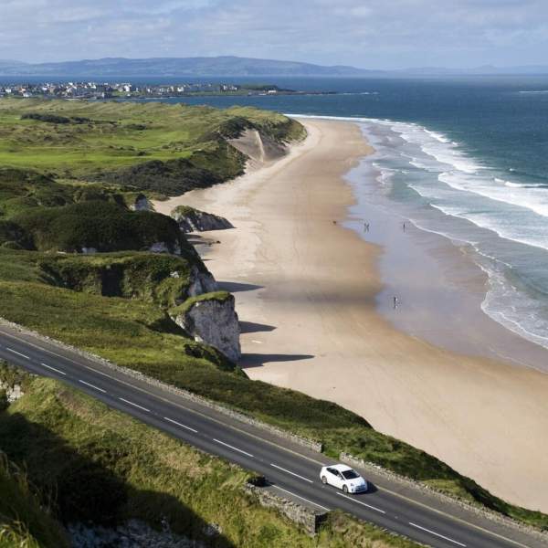 Aerial view of a car along the Causeway Coastal Route on a sunny day with the beach in the background