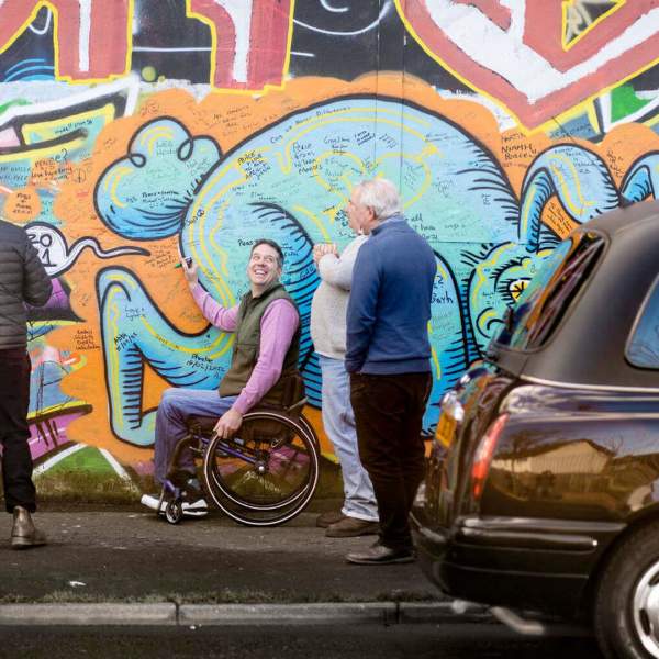 Visitors enjoying signing the Peace Wall in Belfast on a Touring around Belfast black taxi tour