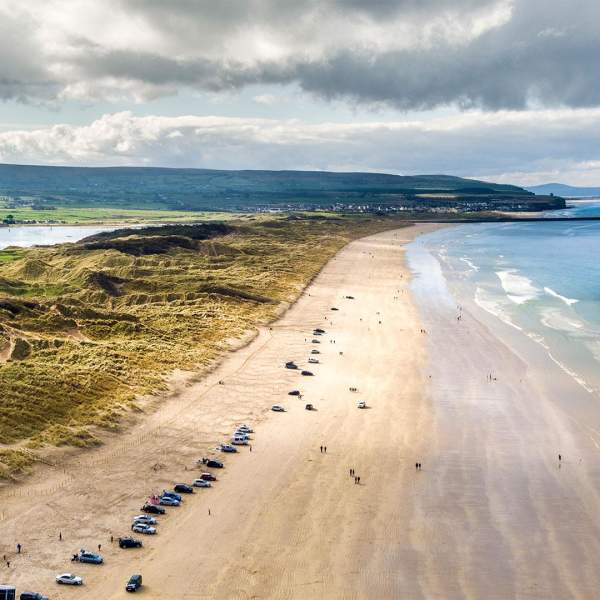 Aerial view of Portstewart beach with cars parked along the stretch of sand.