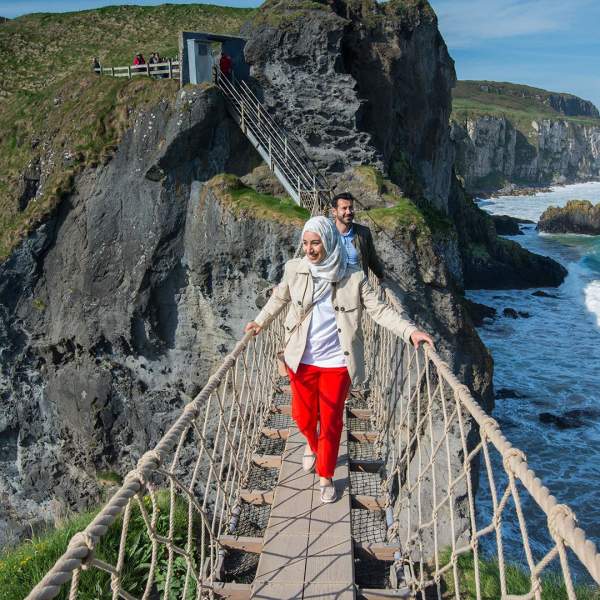 Stunning views of Carrick-a-Rede Rope Bridge, along the Causeway Coastal Route as a couple cross the bridge.