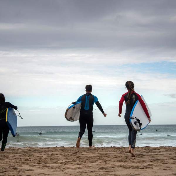 Four surfers running towards the sea to go Surfing at Whiterocks Beach, Portrush, County Antrim